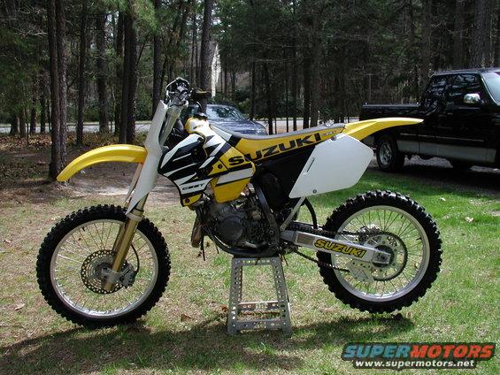 Yellow and white dirt bike on a stand, with trees and a truck in the background