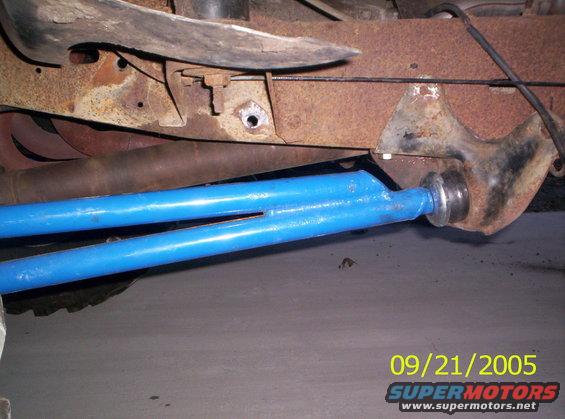 Close-up of blue suspension arm attached to rusty frame with exhaust pipe visible