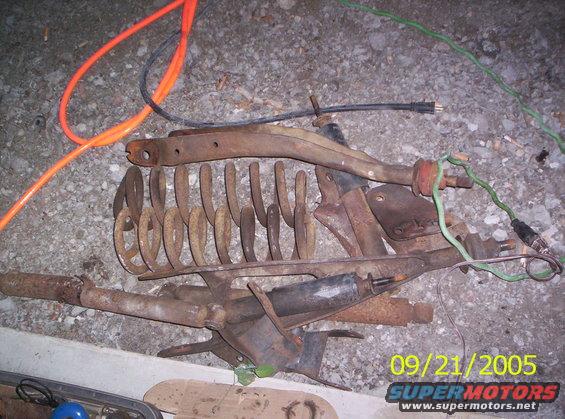 Pile of rusty suspension parts, including springs and control arms, with orange and black cords on the ground