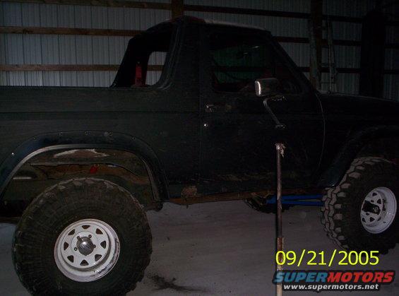Black Ford Bronco with lifted suspension and large tires, seen from the side in a garage