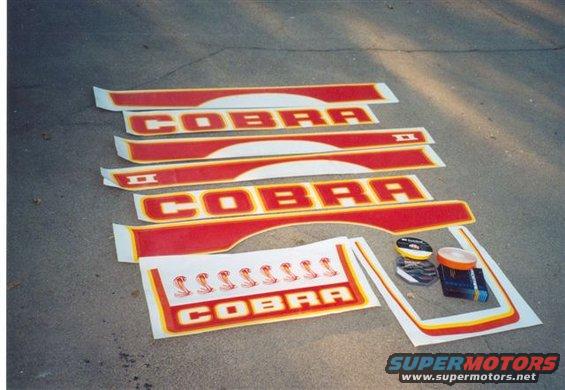 Red and yellow Cobra decals and trim pieces laid out on asphalt, with a small sheet of cobra snake graphics