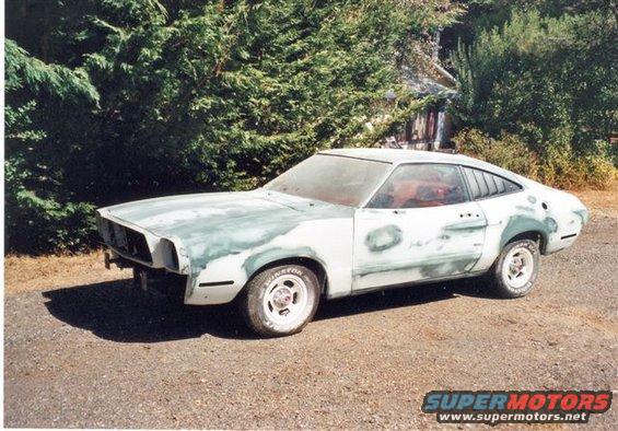1978 Ford Mustang II undergoing bodywork, primer visible on front fenders and doors
