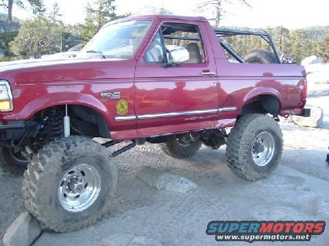 Red 1996 Ford Bronco with lifted suspension and large tires on rocky terrain
