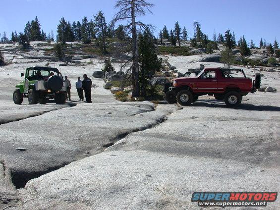 Red 1996 Ford Bronco parked on rocks, 3q-front view. Green Jeep nearby