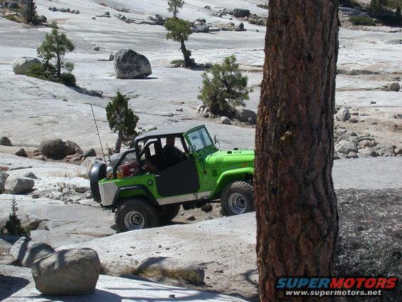 Green off-road vehicle with black doors and a grey top, on a rocky, barren landscape