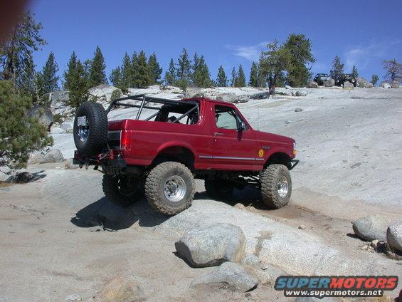 Red 1996 Ford Bronco off-roading on rocks with a spare tire mounted on the rear
