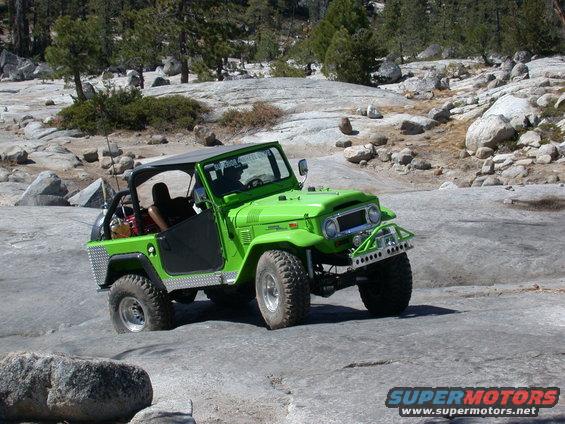 Green Toyota Land Cruiser FJ40 with aftermarket bumper and roll cage driving on rocky terrain
