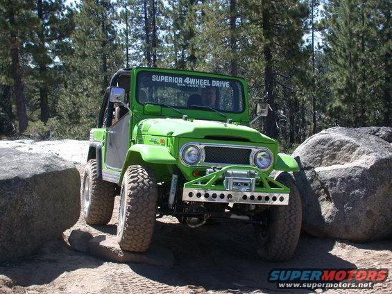 Green off-road SUV with a winch on the front bumper, navigating between large rocks on a dirt trail