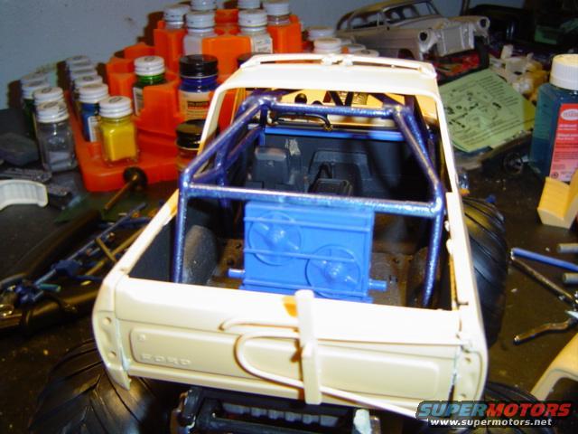 Model truck with roll cage, large tires, and blue engine detail. Beige body shows 'FORD' script