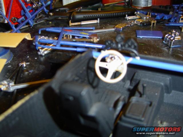 Model car interior parts on a workbench, including a steering wheel and dashboard components