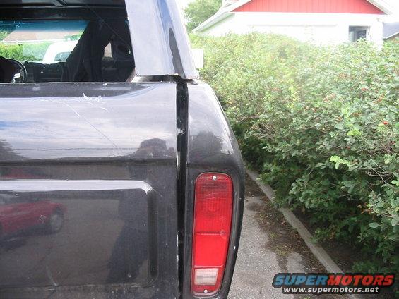 Dark gray 1978 Ford Bronco rear quarter panel and taillight, showing scratches and a reflection of a red car