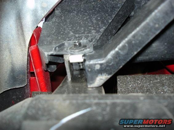 Close-up of a black plastic mounting bracket with a bolt and white clip, attached to red metal