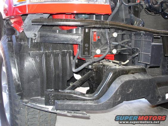 Red vehicle front end structure with black plastic components and metal bracing, viewed from the front