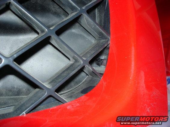Close-up of a black plastic grille with a red body panel on the right