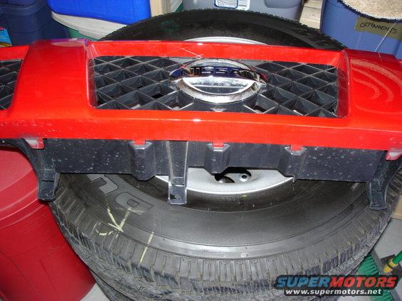 Red Nissan grille with chrome emblem and black diamond pattern, resting on a tire