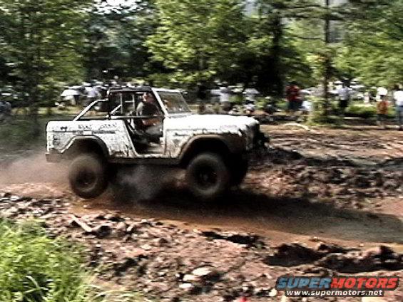 1969 Ford Bronco off-roading through a muddy track with trees in the background