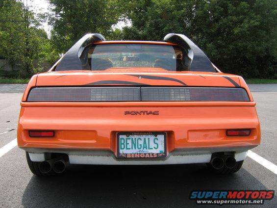 Rear view of orange 1984 Pontiac Fiero with black tiger stripe decals and dual exhaust pipes