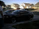 2004 Ford Mustang - A dark 2004 Ford Mustang coupe is parked in a suburban driveway, with other vehicles and houses in the background.