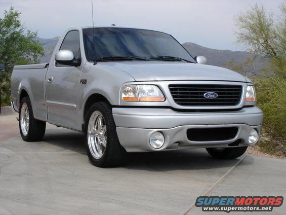 Silver Ford F-150 Lightning pickup truck parked on a concrete driveway with mountains in the background