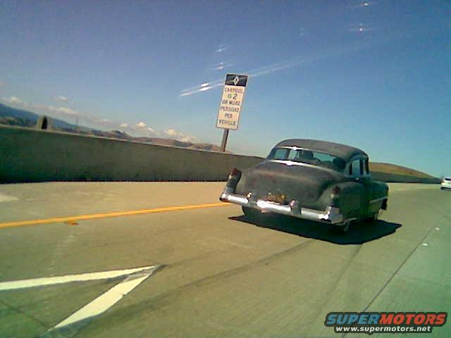 Rear view of a dark colored 1950s sedan driving on a highway