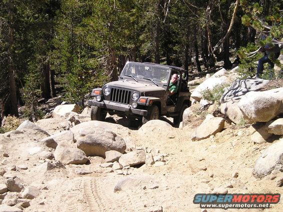 Tan Jeep Wrangler navigating a rocky, off-road trail