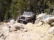 1989 Ford Bronco - A Jeep Wrangler tackles a challenging rocky path in a wooded area.