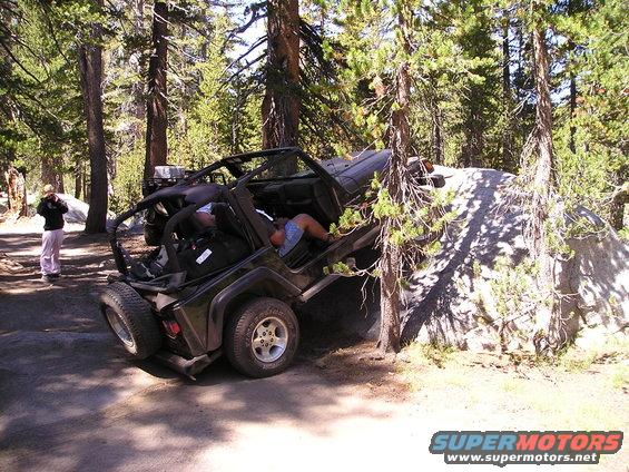 Off-road vehicle wedged between trees and a large rock on a dirt path