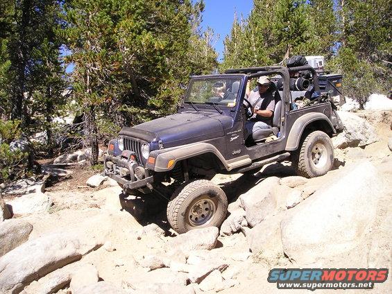 Dark blue Jeep Wrangler TJ navigating a rocky trail, driver visible