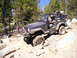 1989 Ford Bronco - Jeep Wrangler TJ tackling a challenging off-road path with large rocks and trees.