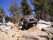 1989 Ford Bronco - A person pushes a Jeep Wrangler through a challenging rocky trail on a sunny day.