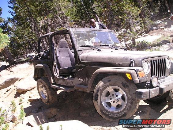 Dark colored Jeep Wrangler TJ with top removed, driving on a rocky mountain trail. Two people are inside