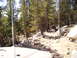 1989 Ford Bronco - A trail winds through a rocky, wooded area, with two vehicles navigating the terrain in the distance.