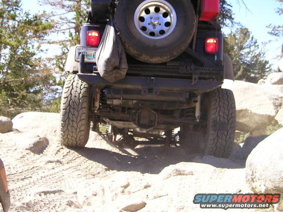 Rear view of a Jeep Wrangler on a rocky trail with a spare tire mounted on the back
