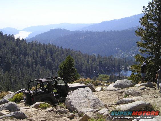 Jeep Wrangler parked on rocky terrain overlooking a lake and forest