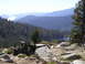 1989 Ford Bronco - Off-road Jeep Wrangler parked on a rocky overlook with a scenic mountain lake and forest view.