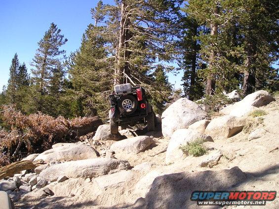 Red Jeep Wrangler navigating a rocky trail, rear view