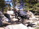 1989 Ford Bronco - A Jeep Wrangler TJ is shown off-roading on a challenging rocky path surrounded by trees and large boulders.