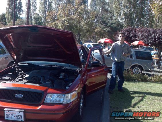 Red Ford Crown Victoria with hood and driver door open, man standing next to it. Another SUV is parked behind