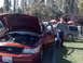 1999 Ford Crown Victoria - A man stands by a red Ford Crown Victoria with its hood and door open, parked outdoors with other vehicles visible.
