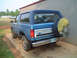 1985 Ford Bronco - A blue Ford Bronco is parked on a concrete pad next to a metal building, with another vehicle visible in the background.