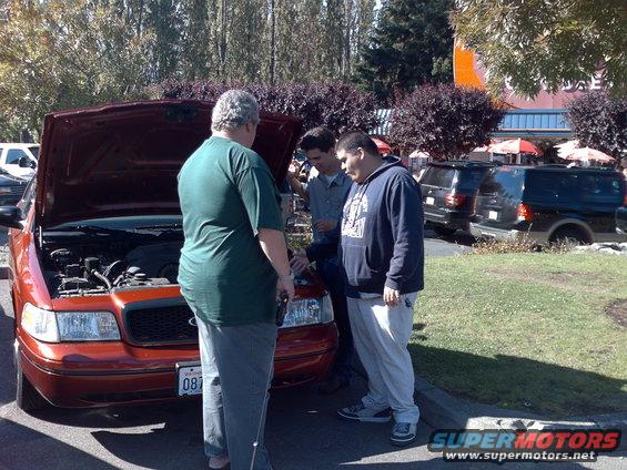 1999 Ford Crown Victoria with hood open, three men gathered around the engine bay