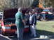 1999 Ford Crown Victoria - Three men examine the engine of a red 1999 Ford Crown Victoria at an outdoor gathering.