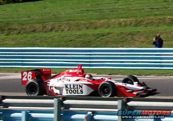 Red and white IndyCar with number 26 and 'KLEIN TOOLS' text, seen from the side on a race track