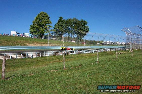 Open-wheel race car on track with spectators and RVs in background