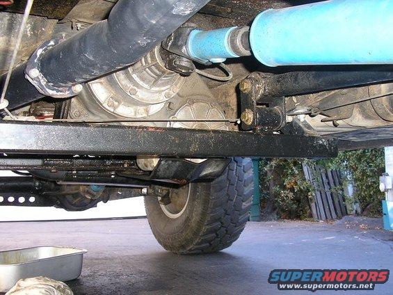 Underside of a vehicle showing the drivetrain, exhaust, and a tire. A drip pan is visible