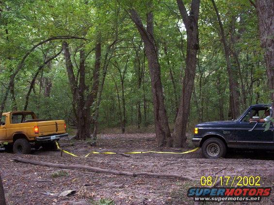 Dark green 1992 Ford F-Series truck pulling a yellow Ford Bronco out of mud in a wooded area