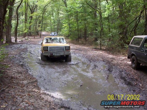 Yellow 1980s SUV navigating a deep mud puddle on a forest trail
