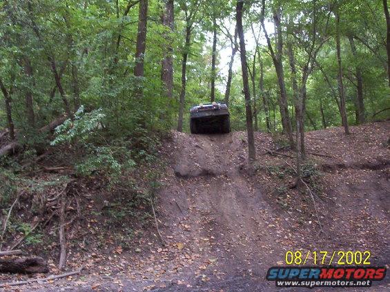 SUV going up a steep dirt hill in woods. Watermark says 08/17/2002 SUPERMOTORS