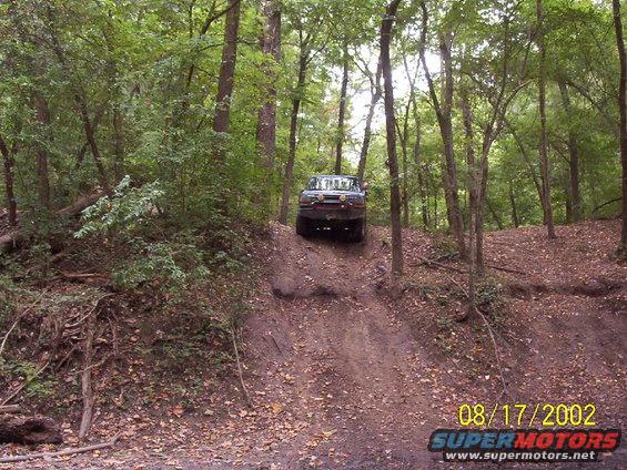 Dark blue 1992 Ford Bronco driving up a dirt hill in a wooded area
