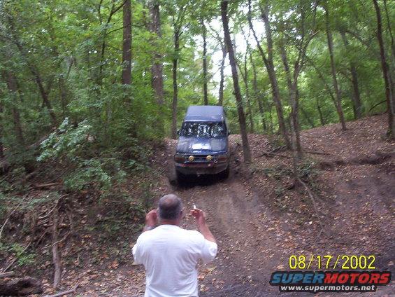 Blue SUV on a wooded trail, man in foreground